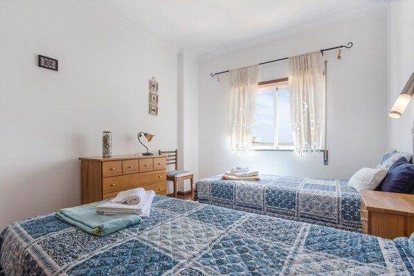Une chambre avec deux lits, une commode, une fenêtre avec des rideaux et une lampe de chevet.