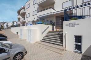 A multi-story residential building with a staircase leading to the entrance, a gated entrance, and a sign indicating the building name and block number.