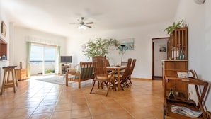 A spacious living area with a dining table, chairs, a ceiling fan, a large window, and a view of the sea. - Pet-Friendly Apartment Your Secret in Lagos (Lagos)