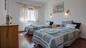 A bedroom with two beds, a wooden dresser, a window with curtains, a wall-mounted lamp, and a painting. - Pet-Friendly Apartment Your Secret in Lagos (Lagos)
