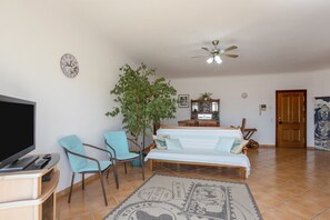 A bedroom with a bed, two chairs, a television, a ceiling fan, a clock, and a door.