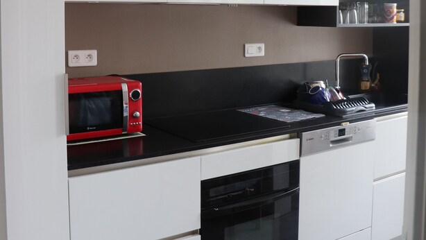A modern kitchen with white cabinets, a black countertop, a red microwave, and a hanging light fixture. - L'havre zen cancalais - Apart peaceful 4 pers tt confort (Cancale)