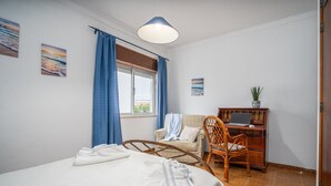 Een slaapkamer met een bed, een bureau met een laptop, een stoel en een raam met gordijnen.