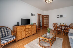 A living room with a television, wicker furniture, a dining area with a table and chairs, and a door leading to another room.