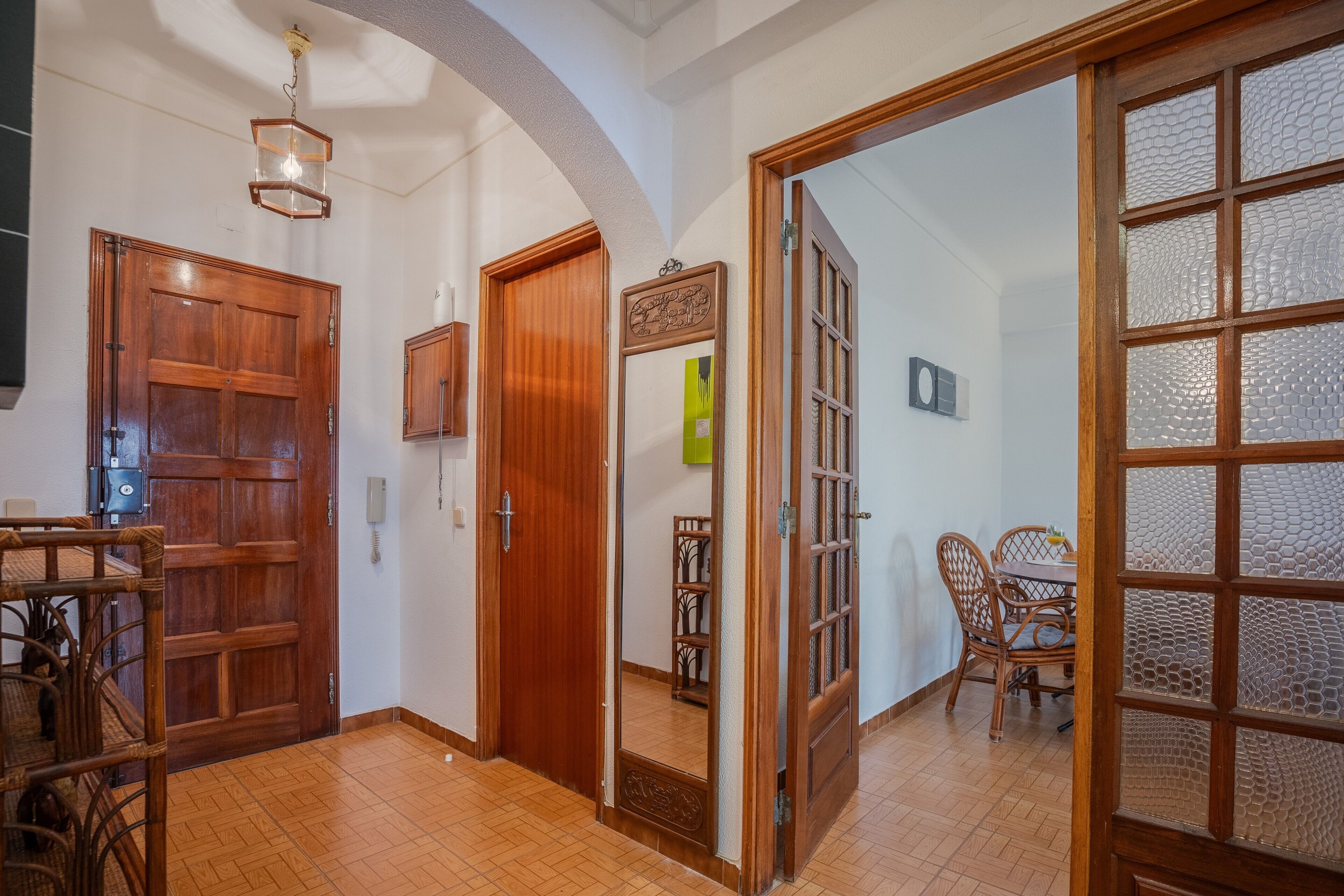 A hallway with wooden doors, a dining area with wicker furniture, and a tiled floor.
