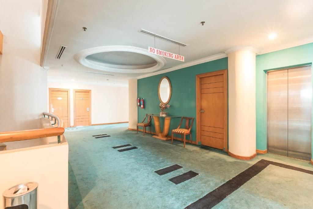 A hotel lobby with a 'NO SMOKING AREA' sign, a reception desk, a mirror, a wooden door, and an elevator.