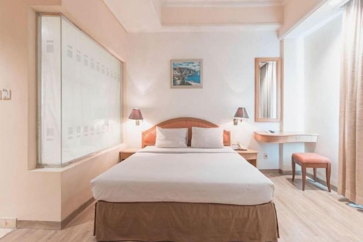 A hotel room with a bed, bedside tables, a desk, and a window.
