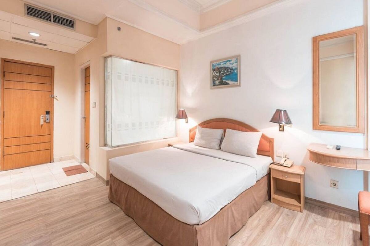 A hotel room with a large bed, bedside lamps, a desk, and a window with a view.