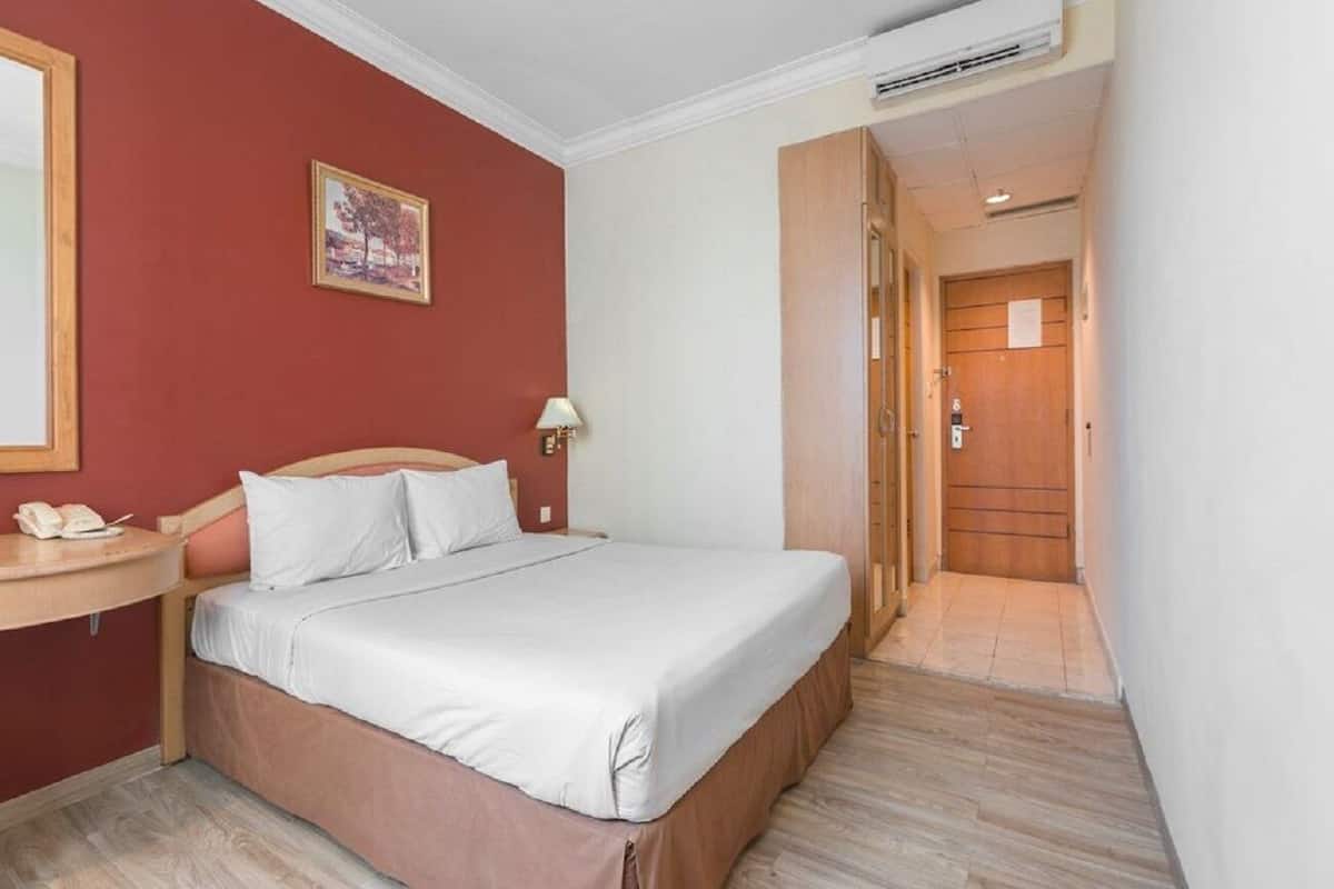 A hotel room with a bed, a bedside table with a lamp, and a wooden door leading to a hallway.