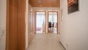 Un pasillo con puertas de madera, un comedor con sillas y una mesa, y un cuadro en la pared.