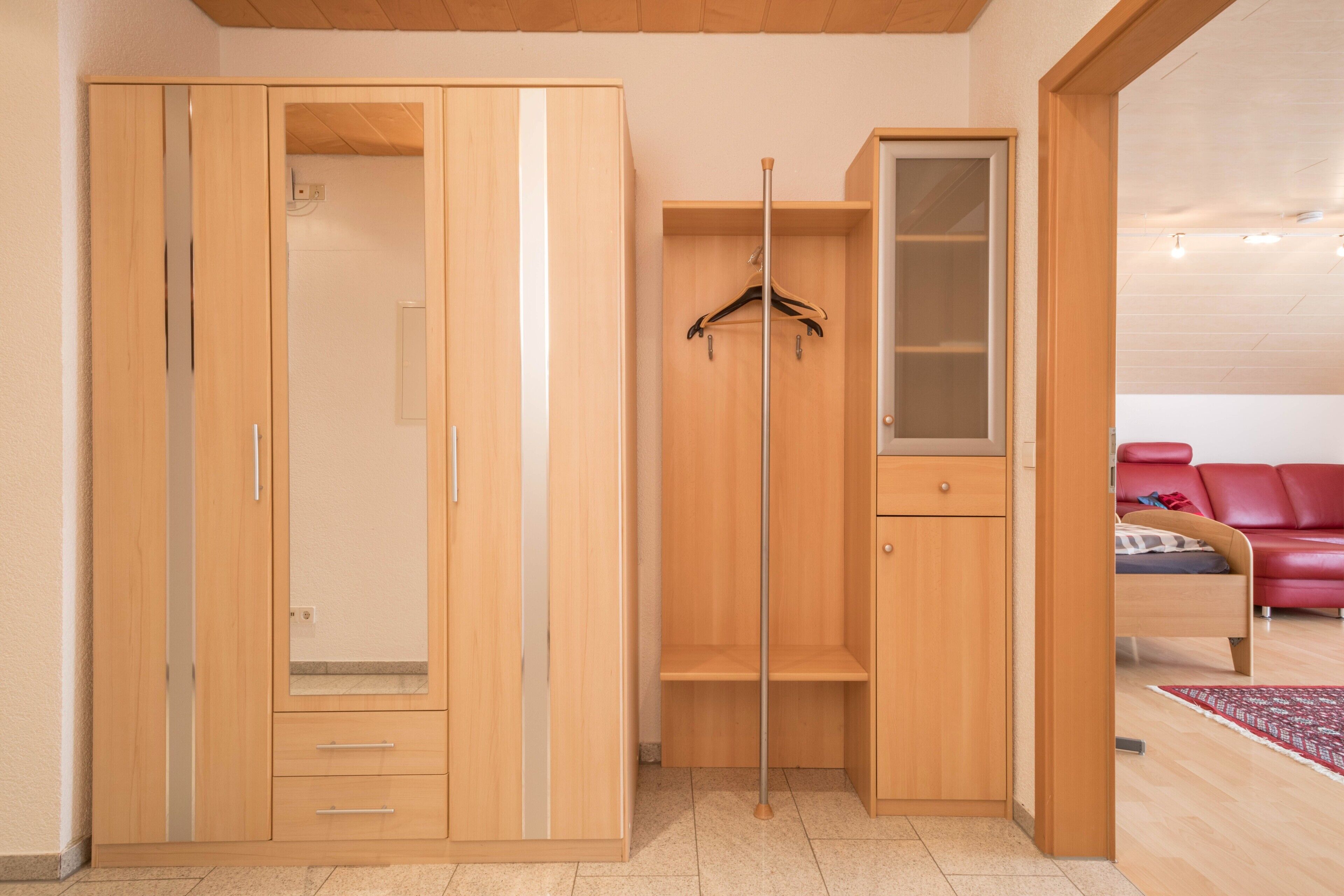 Een kamer met een houten garderobe, een kledingroede en een bed met een rode hoofdeinde.