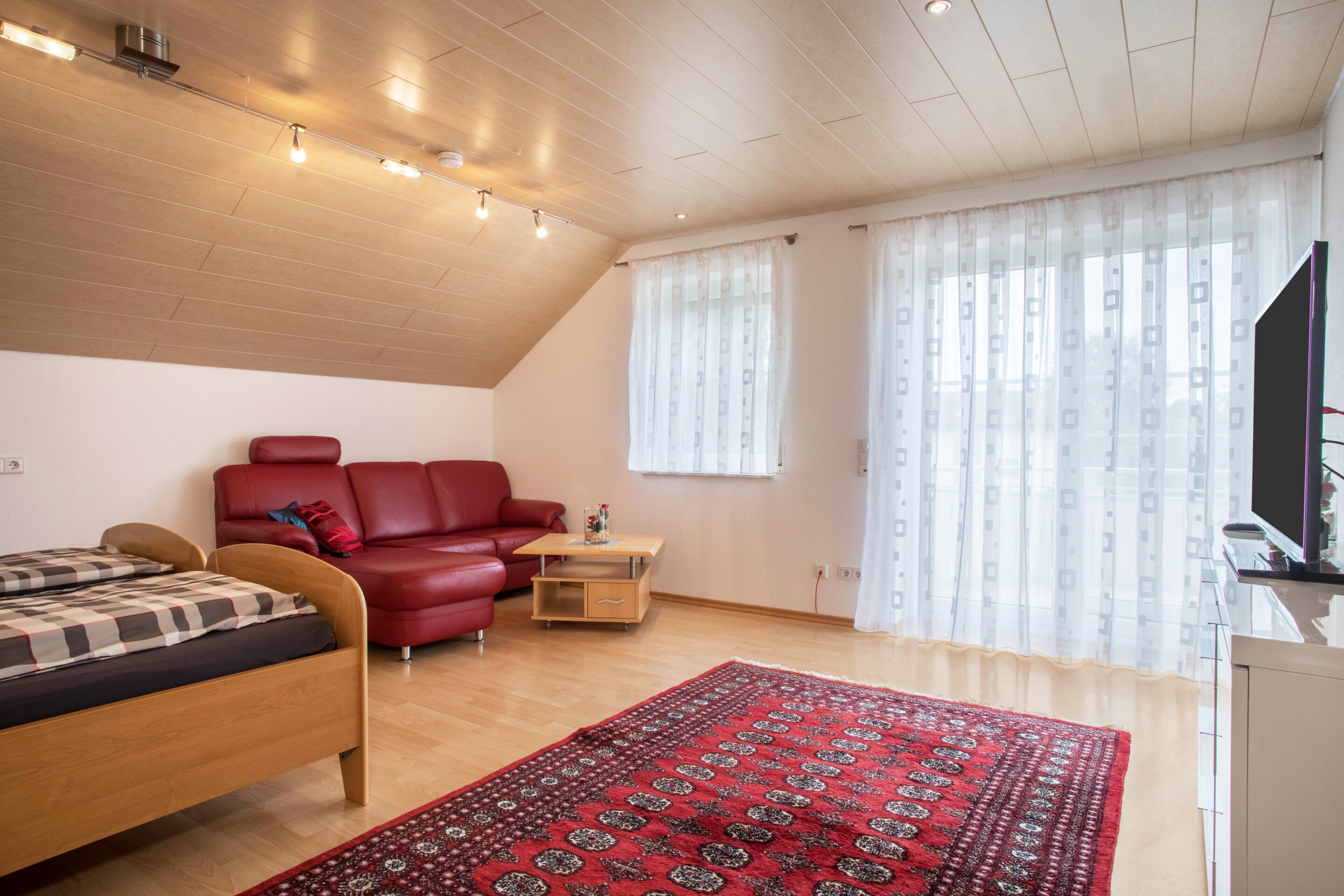Ein Zimmer mit einem Bett, einem roten Schlafsofa, einem kleinen Tisch und einem Fernseher.