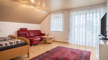 Ein Zimmer mit einem Bett, einem roten Schlafsofa, einem kleinen Tisch und einem Fernseher.