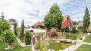 Un jardín con un estanque, un puente de madera y casas al fondo.