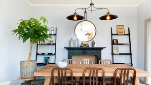 Comedor con mesa de madera, cuatro sillas, una planta en maceta grande, un espejo y dos lámparas colgantes.