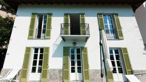 Un edificio de dos pisos con contraventanas verdes, un balcón y fachada de piedra.