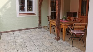 Huoneessa on puinen pöytä ja tuolit, ikkuna ja ovi, ja lattia on laatoitettu.