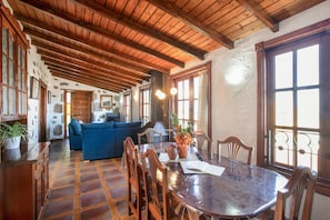 A rustic interior with wooden beams, a round dining table, and a blue sofa. - Holiday Home "Casa Pedro" with Terraces, Panoramic Sea View and Wood Stove (Icod de los Vinos)