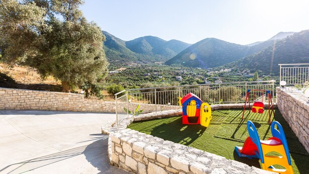 A playground with colorful play structures, surrounded by a stone wall and a view of a valley with mountains in the background. - Paris Villa, with Pool, BBQ, Playground & SeaViews (Bali)