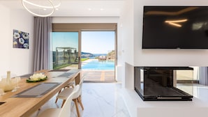 Een moderne woonkamer met een grote televisie, een houten eettafel en uitzicht op een buitenzwembad.