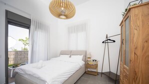 A modern bedroom with a large bed, a wooden wardrobe, a bedside table with a lamp, and a view of the outdoors.