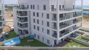 A multi-story hotel with balconies, a swimming pool, and a view of the beach.