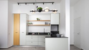 A modern kitchen with white cabinetry, a central island, and a black countertop. There are shelves with plants and kitchenware. - Chic Sea View Balcony Escape by Sea N' Rent (Nahariya)