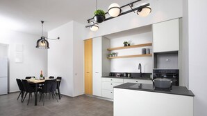 A modern kitchen with white cabinets, a black countertop, and a built-in oven. There is a dining area with a table and chairs. - Chic Sea View Balcony Escape by Sea N' Rent (Nahariya)