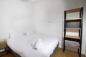A neatly made bed with white linens and a rolled towel, a wooden ladder shelf with towels, and a small bedside table with drawers. - Chic Sea View Balcony Escape by Sea N' Rent (Nahariya)
