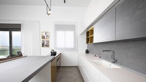 Une cuisine moderne dotée d’un îlot central, de meubles blancs et d’une grande fenêtre offrant une vue dégagée.