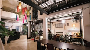 A spacious indoor area with a long table and chairs, a reception desk, and hanging decorative lanterns.
