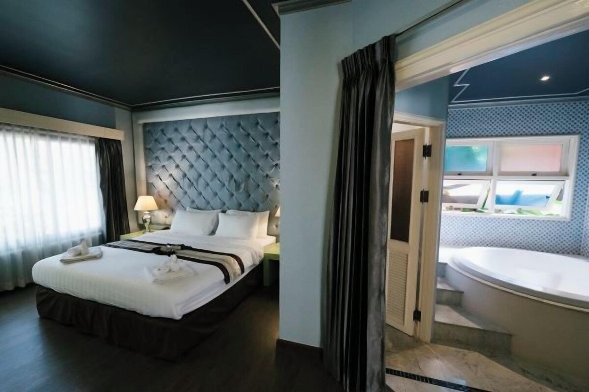 A hotel room with a large bed, a headboard, a nightstand, and a view of a bathroom with a bathtub.