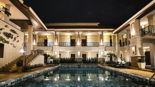 A hotel with a large outdoor swimming pool, multiple balconies, and a well-lit facade.