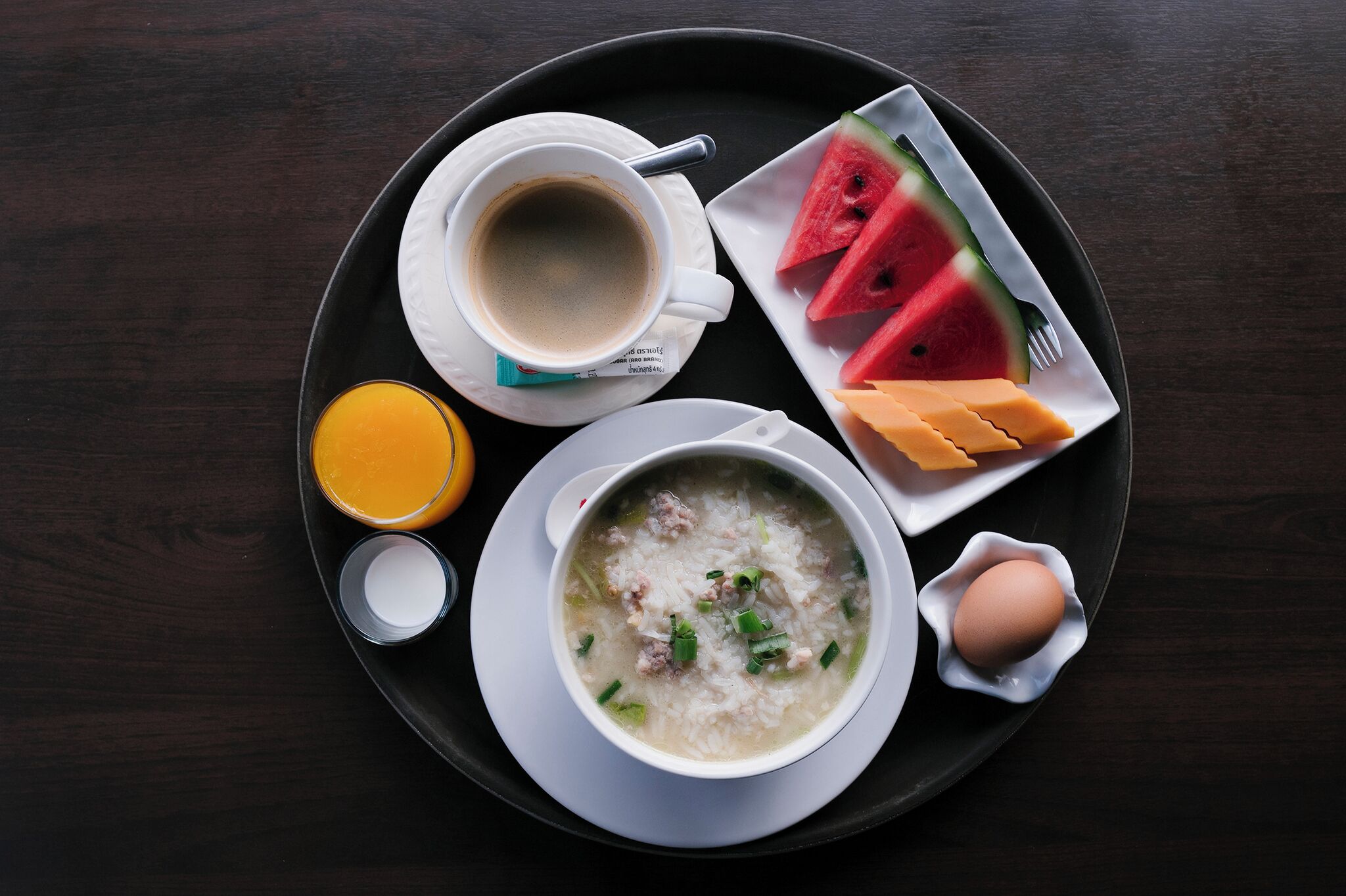 Una bandeja con una taza de café, un plato de sopa, una porción de sandía, queso y un huevo.