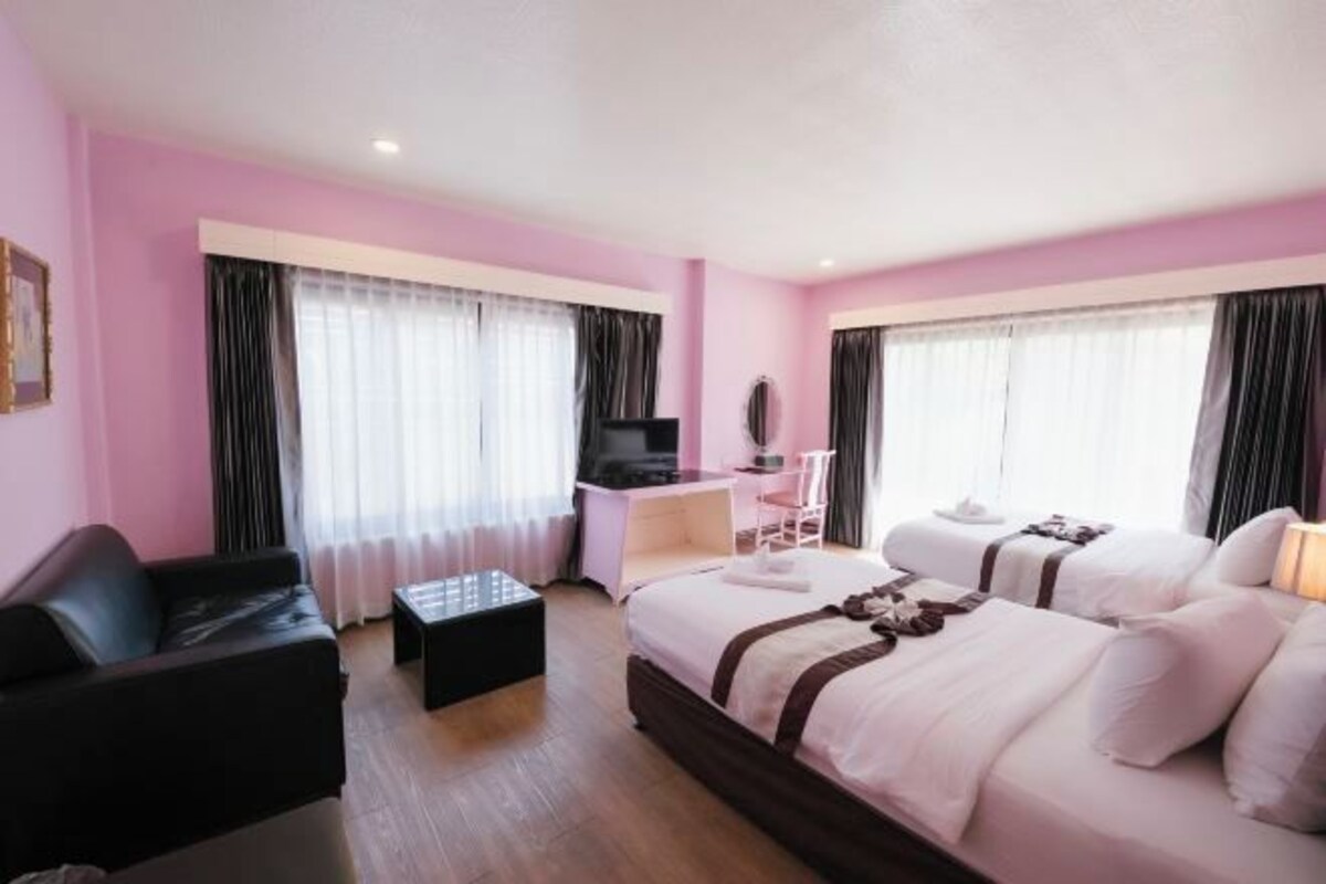 Habitación de hotel con paredes rosas, dos camas, un escritorio, una silla, un televisor y una ventana con cortinas.