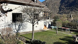 A house with a sloped roof, a visible chimney, and a small garden with a lawn and a tree. - House with large, quiet garden and beautiful mountain views (ANTIGNAC)