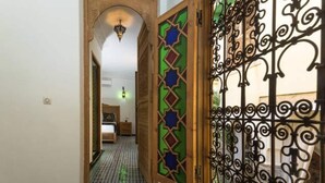A hallway with a bed, a patterned floor, and a decorative door with geometric designs. - Riad Vega. A haven of peace in the heart of the medina (Fès)