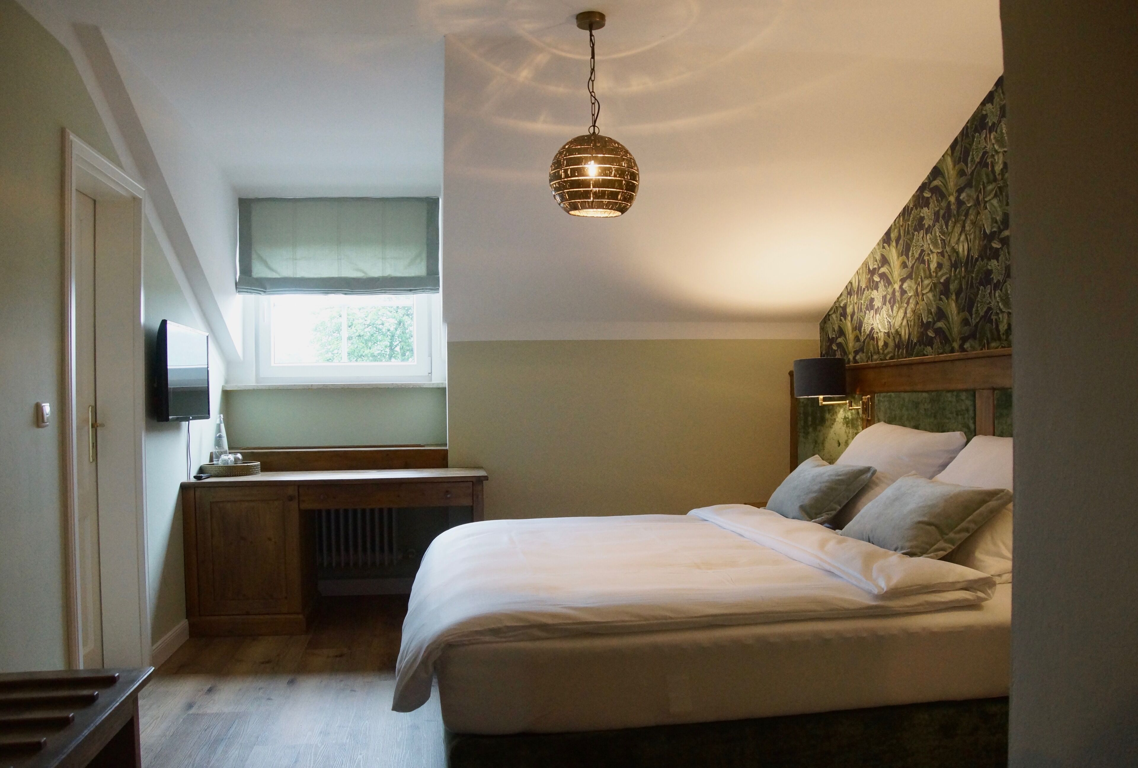 A bedroom with a bed, a desk, a television, and a window.