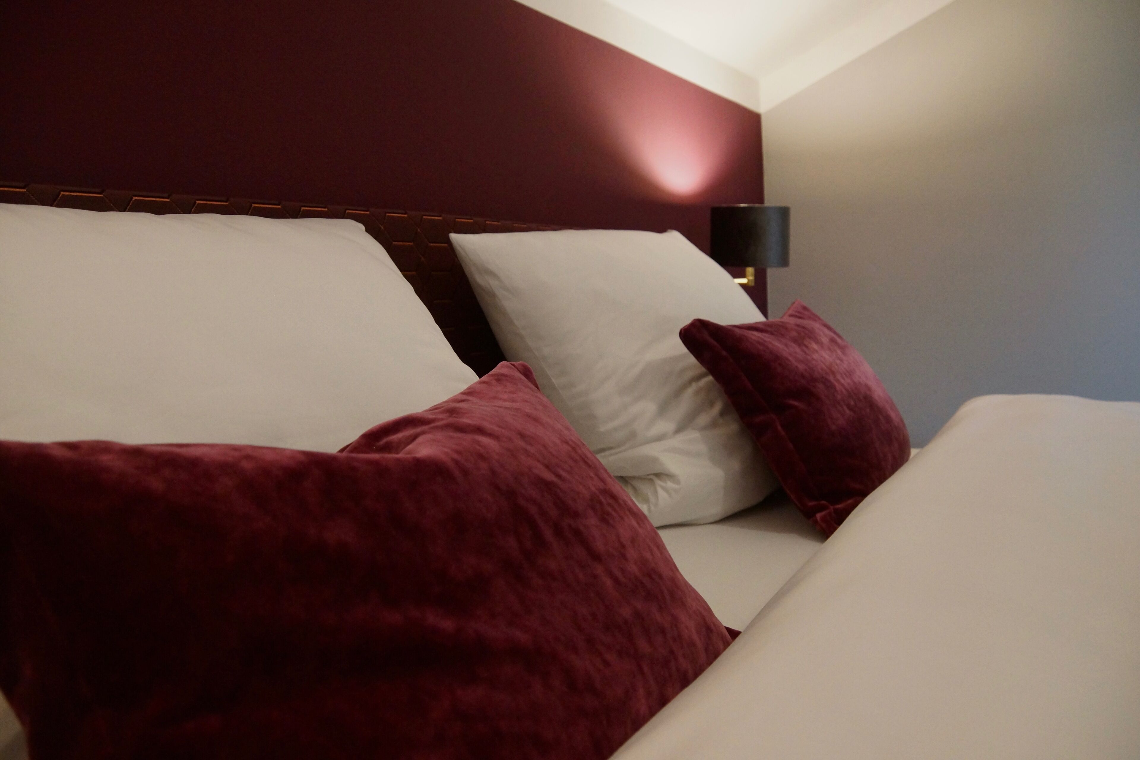 A bed with white and maroon pillows, a dark headboard, and a bedside lamp.