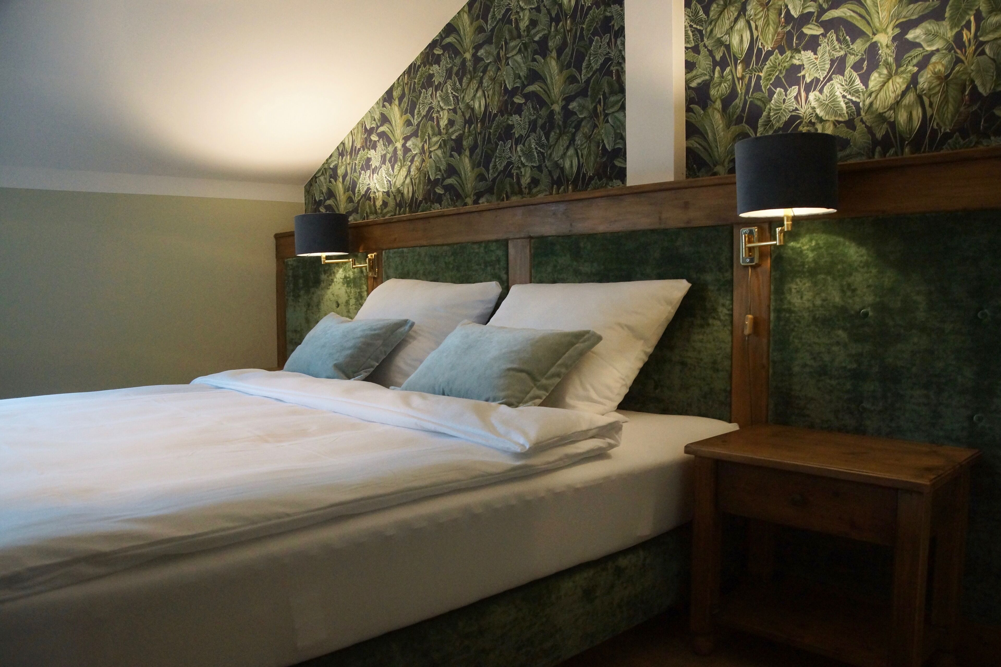 A bedroom with a bed, two bedside tables, and a headboard with a floral wallpaper design.