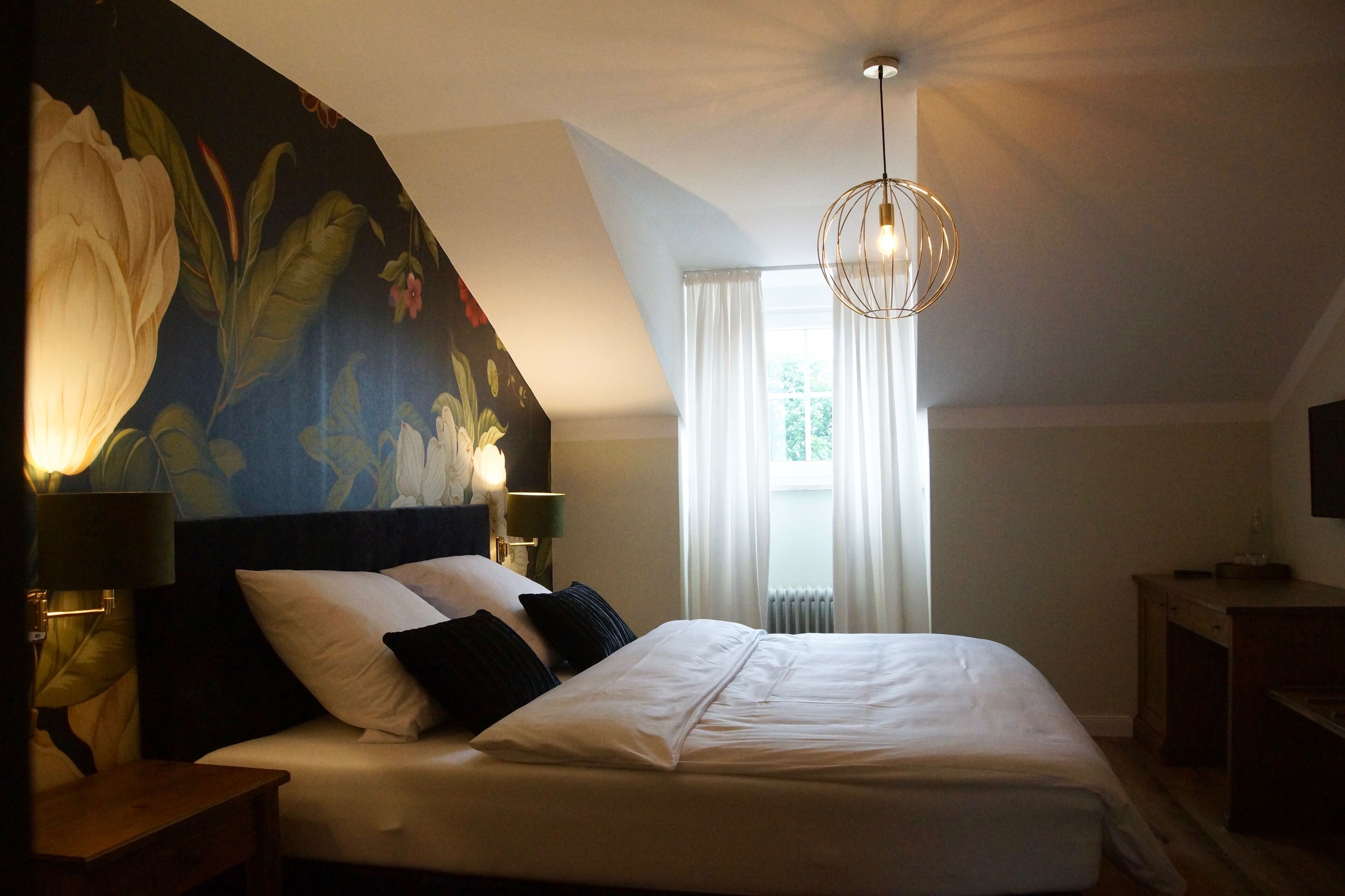 Un dormitorio con una cama grande, una mesita de noche, un televisor montado en la pared y un candelabro en el techo.