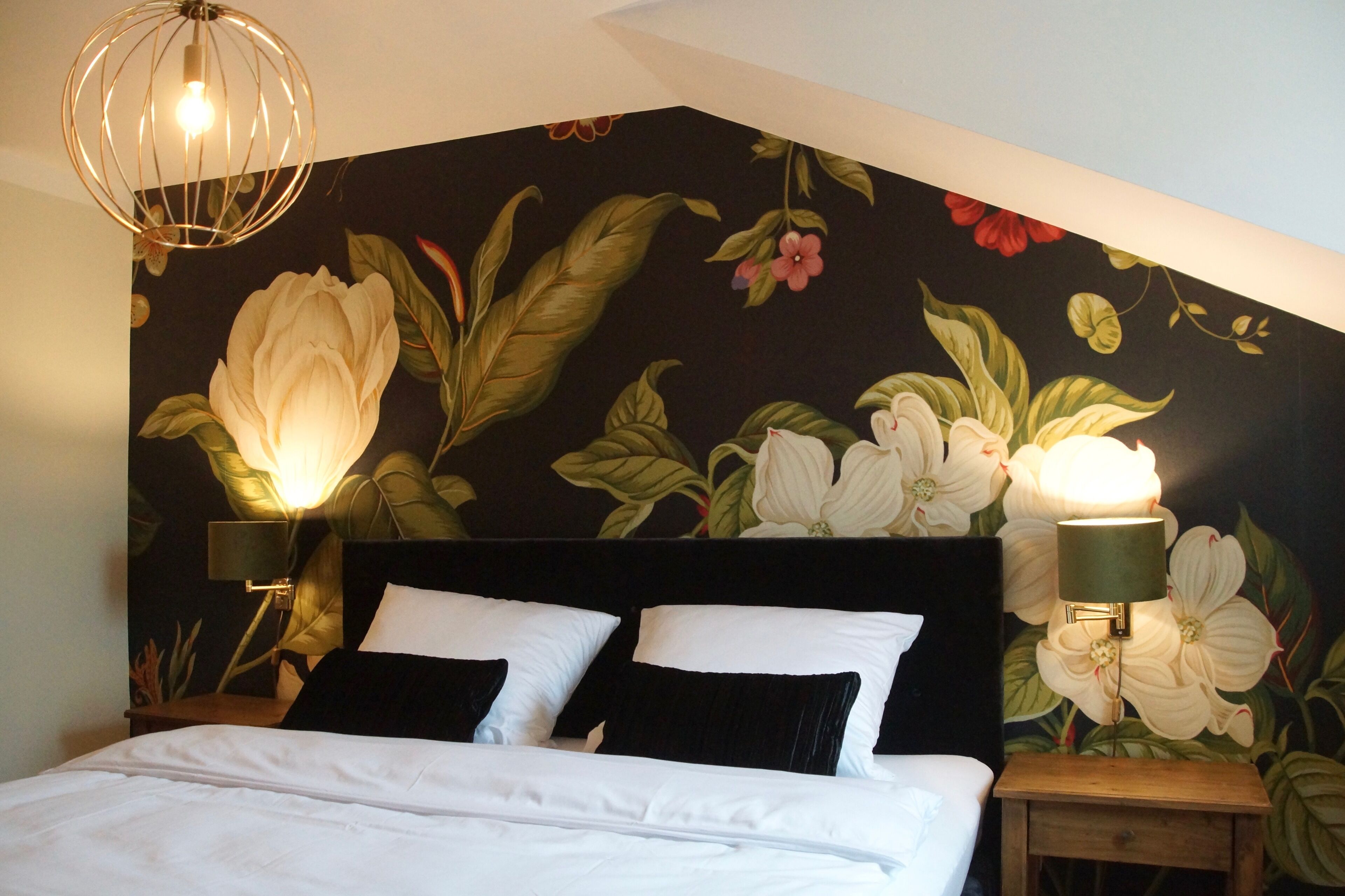 A bedroom with a large bed, two bedside lamps, and a floral mural on the wall.