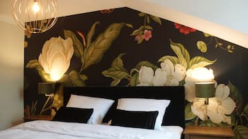 A bedroom with a large bed, two bedside lamps, and a floral mural on the wall.