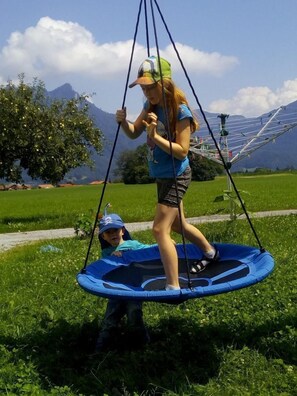 Une personne est assise sur une balançoire dans un espace verdoyant, avec des montagnes en arrière-plan.