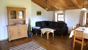 Uma sala de estar acolhedora com teto de madeira, sofá escuro, um armário de madeira e uma mesa de jantar com cadeiras.