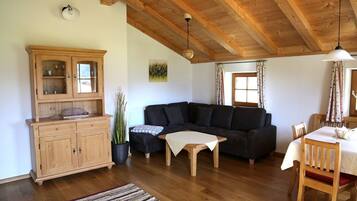 Ein gemütliches Wohnzimmer mit Holzboden, einem dunkelbraunen Sofa, einem Holzschrank und einem Esstisch mit Stühlen.