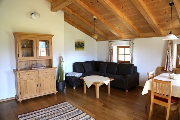 Un salon chaleureux avec un plafond en bois, un canapé de couleur sombre, un meuble en bois et une table à manger avec des chaises.