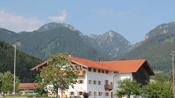 Ein zweistöckiges Gebäude mit rotem Ziegeldach, umgeben von üppiger Vegetation und Bergen im Hintergrund.