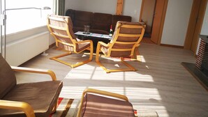 Ein Wohnzimmer mit einer Couch, zwei Holzstühlen, einem Tisch und einer Pendelleuchte.
