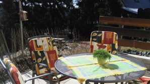 Ein runder Metalltisch mit kariertem Tischtuch und einer Topfpflanze, umgeben von bunten Stühlen mit Blumenmuster.